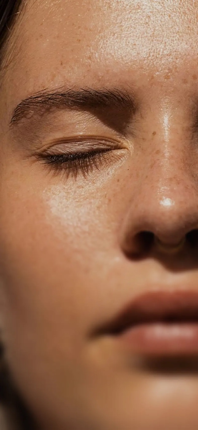 Close-up of a Thea member with freckles, eyes closed, in warm light